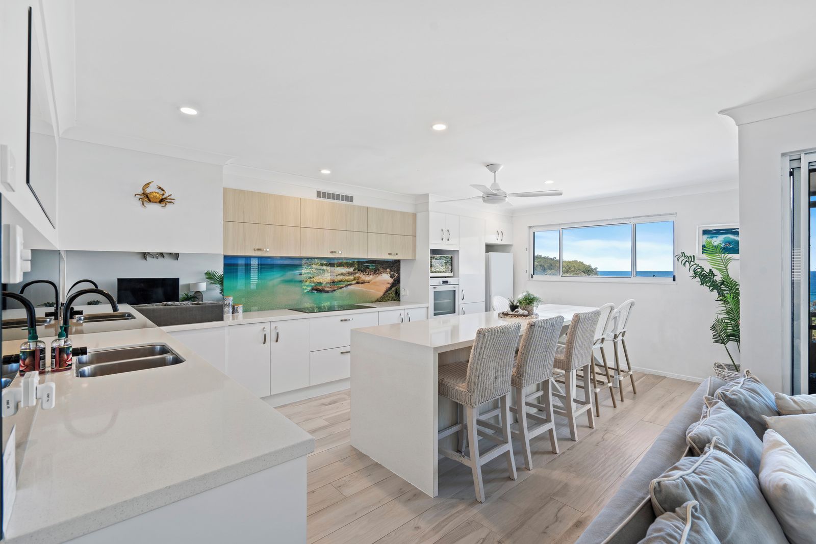 A modern kitchen with a large island, white cabinetry, and a scenic ocean view through the window.