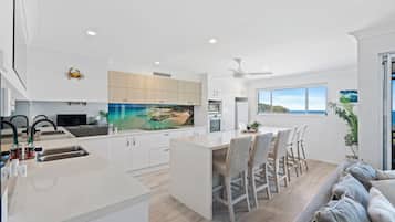 A modern kitchen with a large island, white cabinetry, and a scenic ocean view through the window.