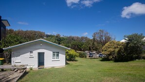 A small white single-story house with a gabled roof, a front door, and a small porch area. - Cabana - One of the only original Straddie beach shacks left standing. (Point Lookout)