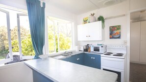 A kitchen with a large island, white cabinets, a microwave, an oven, and a window with blue curtains. - Cabana - One of the only original Straddie beach shacks left standing. (Point Lookout)