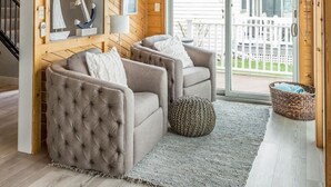 Une pièce chaleureuse avec un plafond en bois, un ventilateur de plafond, une grande fenêtre et une vue sur une clôture blanche à l’extérieur.