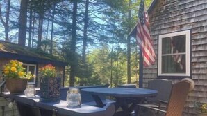 Une cabane en bois avec une terrasse, une table, des chaises et une plante en pot.
