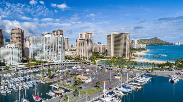A marina with numerous boats docked, surrounded by high-rise buildings and a beach in the background.