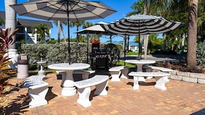 Mobilier d’extérieur pour terrasse, comprenant des tables et des bancs, entouré de palmiers et agrémenté d’un barbecue.