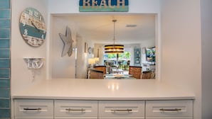 Een keuken met een wit aanrecht, een hangend bordje met de tekst 'BEACH', een zeester decoratie en een uitzicht op de eetruimte.