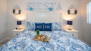 A bedroom with a bed, two nightstands, a wall-mounted sign reading "SIESTA" with star decorations, and a breakfast tray on the bed.