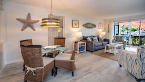 Een woonkamer met een eethoek, met rieten meubels, een glazen tafel en een zeester decoratie.