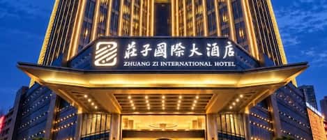 Exterior del Hotel Zhuang Zi International, con una entrada destacada y señalización iluminada.