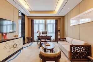 A modern hotel room with a flat-screen TV, a sofa, a dining table with chairs, and a decorative screen. - Zhuangzi International Hotel (Mengcheng)