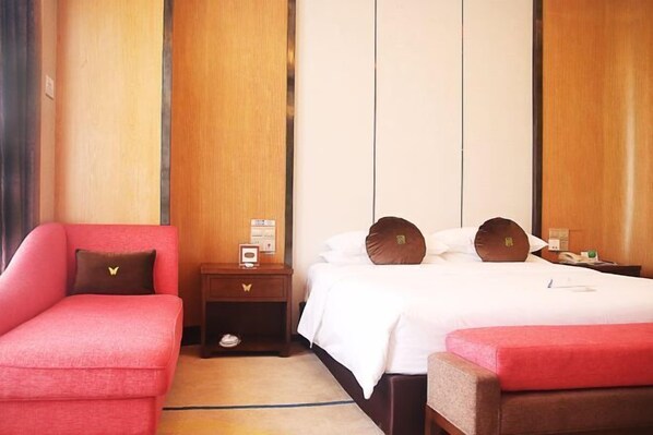 Una habitación de hotel con una cama, un sillón rojo, una mesita de noche de madera y una pequeña mesa.