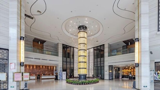 A spacious lobby with a central pillar, a reception desk, and a seating area. - Zhuangzi International Hotel (Mengcheng)
