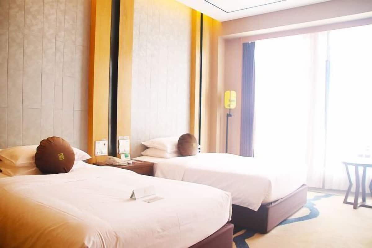Une chambre d’hôtel avec deux lits, une petite table et une fenêtre avec des rideaux.