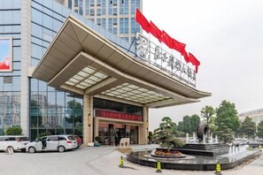 A modern building with a large entrance, a fountain, and red flags. - Zhuangzi International Hotel (Mengcheng)
