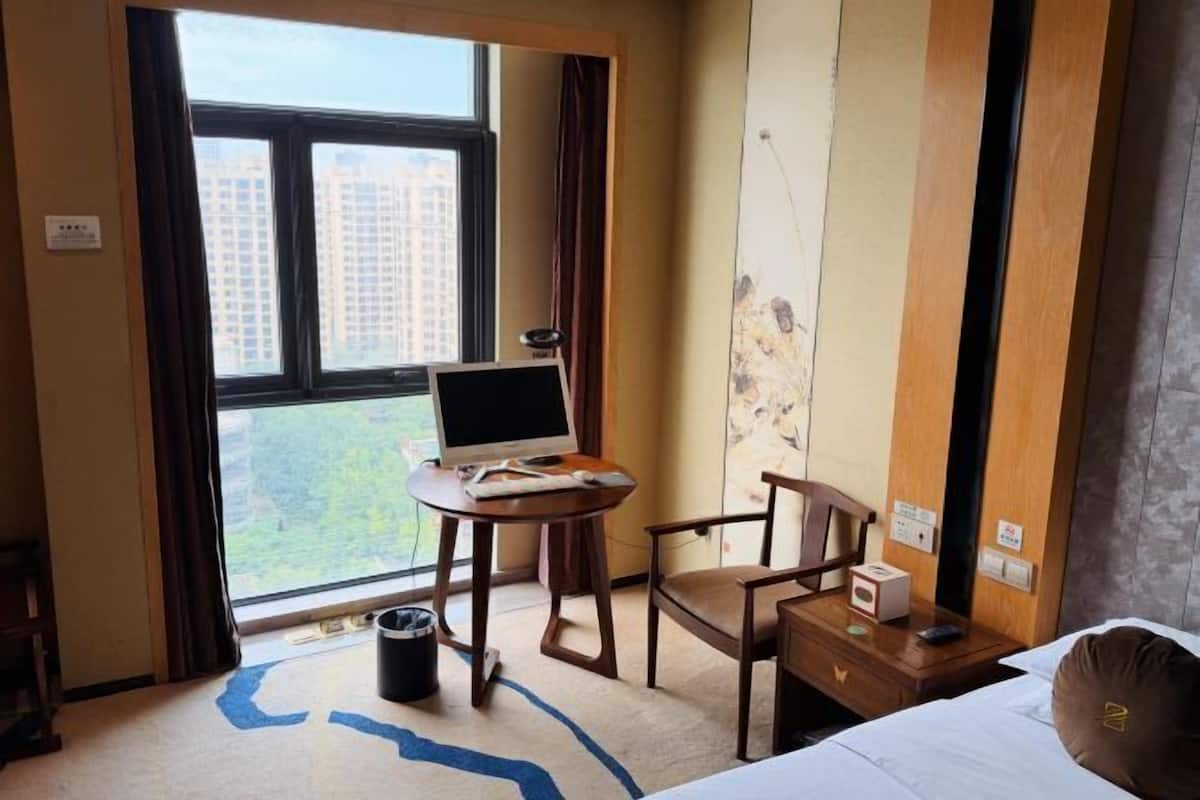 Une chambre d’hôtel avec une grande fenêtre, un bureau avec un ordinateur, une chaise, une table de chevet et un lit.
