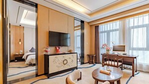 A hotel room with a bed, a TV, a desk with a computer, and a dining area with chairs. - Zhuangzi International Hotel (Mengcheng)