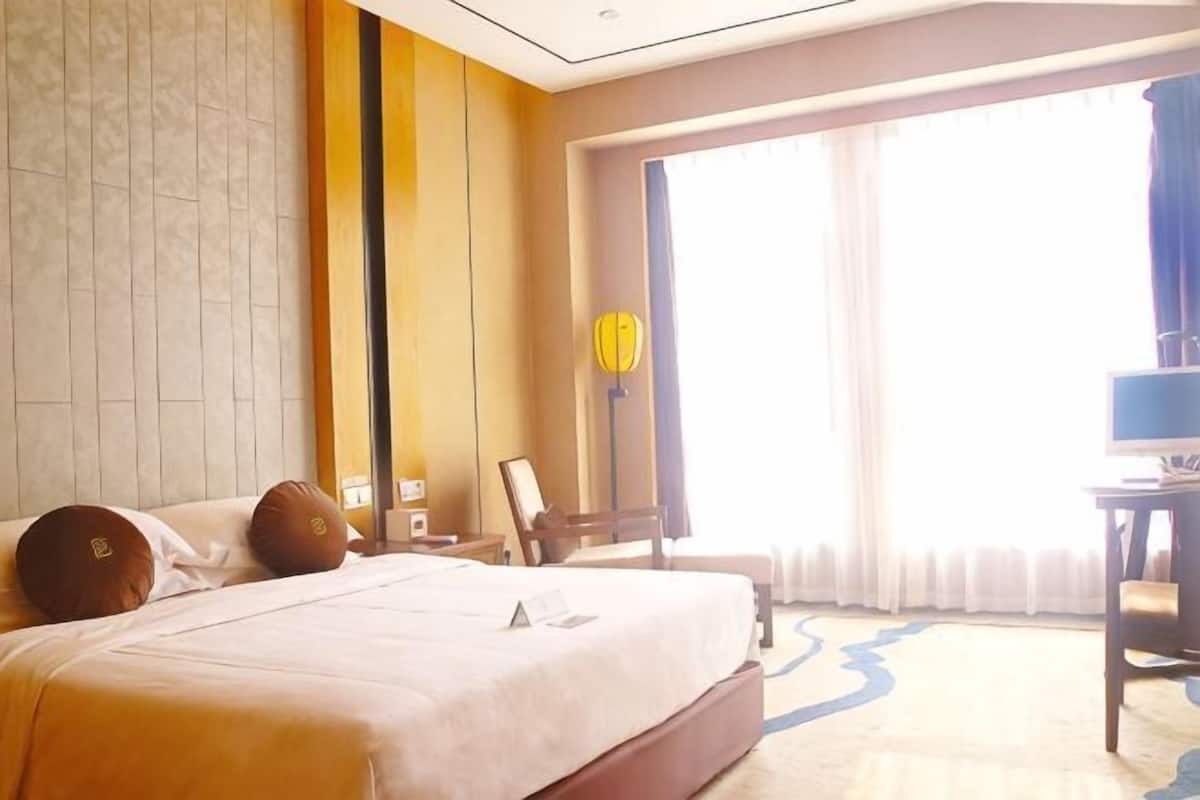 Une chambre d’hôtel avec un grand lit, un bureau, une chaise et une vue sur l’extérieur.