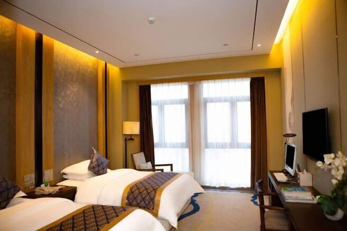 Une chambre d’hôtel avec deux lits, un bureau avec un ordinateur, une télévision et une grande fenêtre avec des rideaux.
