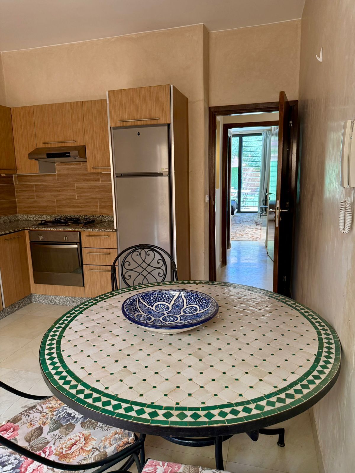 A kitchen with a refrigerator, oven, and stove. There's a dining table with a decorative bowl and chairs.