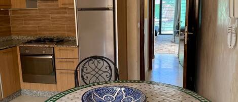 A kitchen with a refrigerator, oven, and stove. There's a dining table with a decorative bowl and chairs.