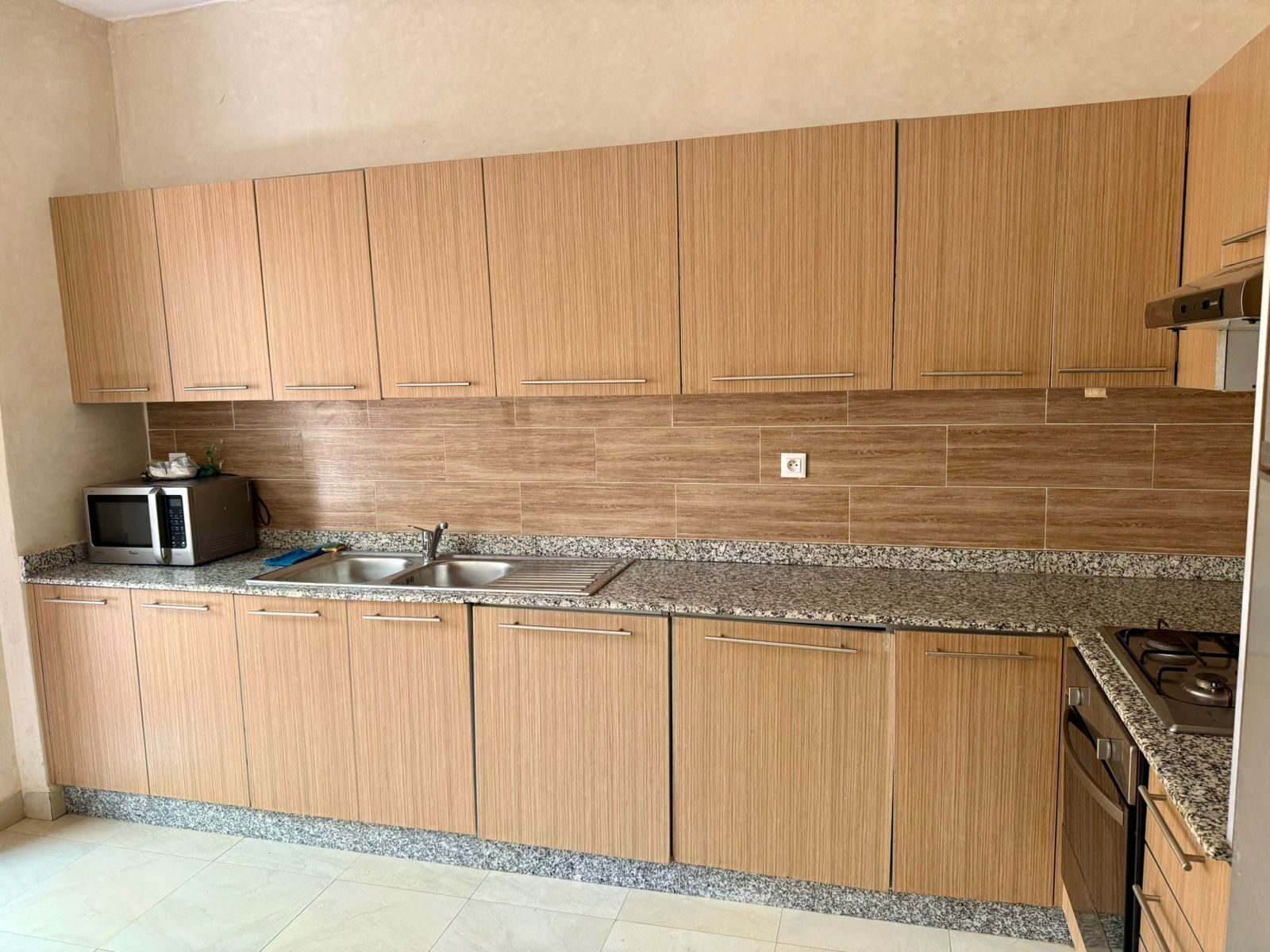 Una cocina con armarios de madera, encimeras de granito, un microondas, un fregadero y una estufa.