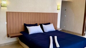 Una cama grande con cabecera de madera, dos mesitas de noche y dos lámparas de pared.