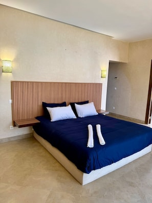 A large bed with a wooden headboard, two bedside tables, and two wall-mounted lights. - Best 2Bd Room Villa in Al Maaden (Marrakesh-Safi)