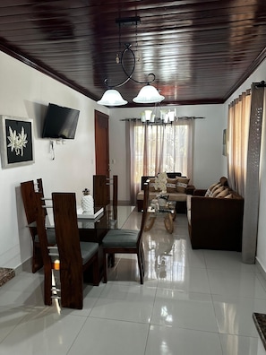 A modern living room with a dining area, a flat-screen TV, and a chandelier.