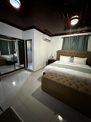 Een slaapkamer met een groot bed, een nachtkastje, een spiegel en een schuifglazen deur die leidt naar een balkon.