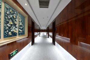 A corridor with wooden paneling, a carpeted floor, and a sign indicating the direction to the bathroom. - Wanhao Hotel (Hailun)