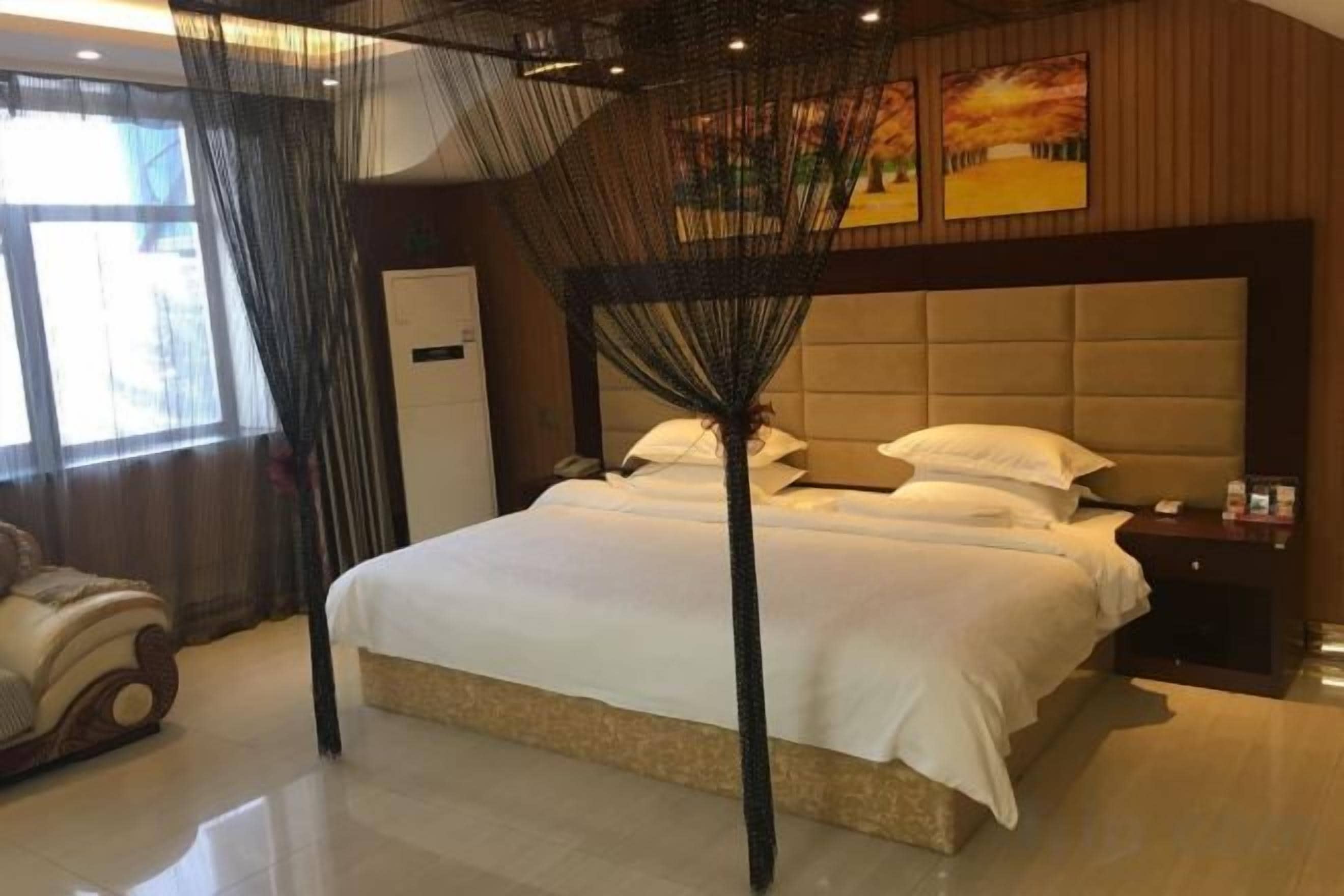A hotel room with a large bed, a bedside table, a nightstand, a wardrobe, and a window with curtains.