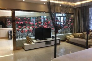 A modern living room with a flat-screen TV on a white console, a sofa, and a decorative wall with floral patterns. - Wanhao Hotel (Hailun)