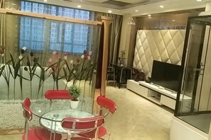 A modern living room with a glass partition, a round glass table, red chairs, a TV, and a cushioned seating area. - Wanhao Hotel (Hailun)