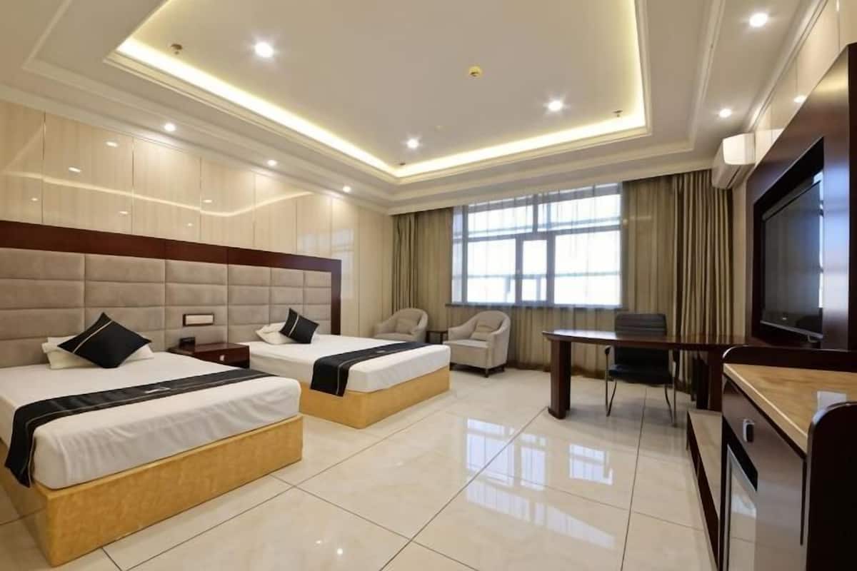 Habitación de hotel con dos camas, un escritorio, televisor y un ventanal amplio.