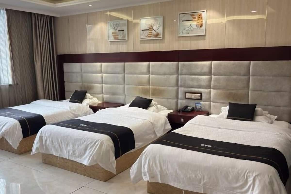 Habitación de hotel con tres camas, un cabecero grande y acolchado, y obras de arte en las paredes.