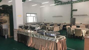 Un salón de banquetes con varias mesas y sillas, montaje tipo buffet y un amplio ventanal.