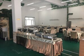 A banquet hall with multiple tables and chairs, buffet setup, and a large window. - Wanhao Hotel (Hailun)