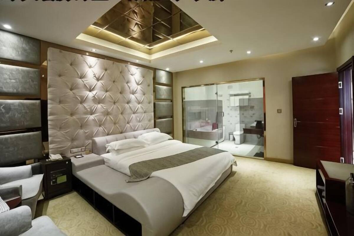 Un dormitorio con una cama grande, una mesita de noche, un armario y un baño con mampara de vidrio.
