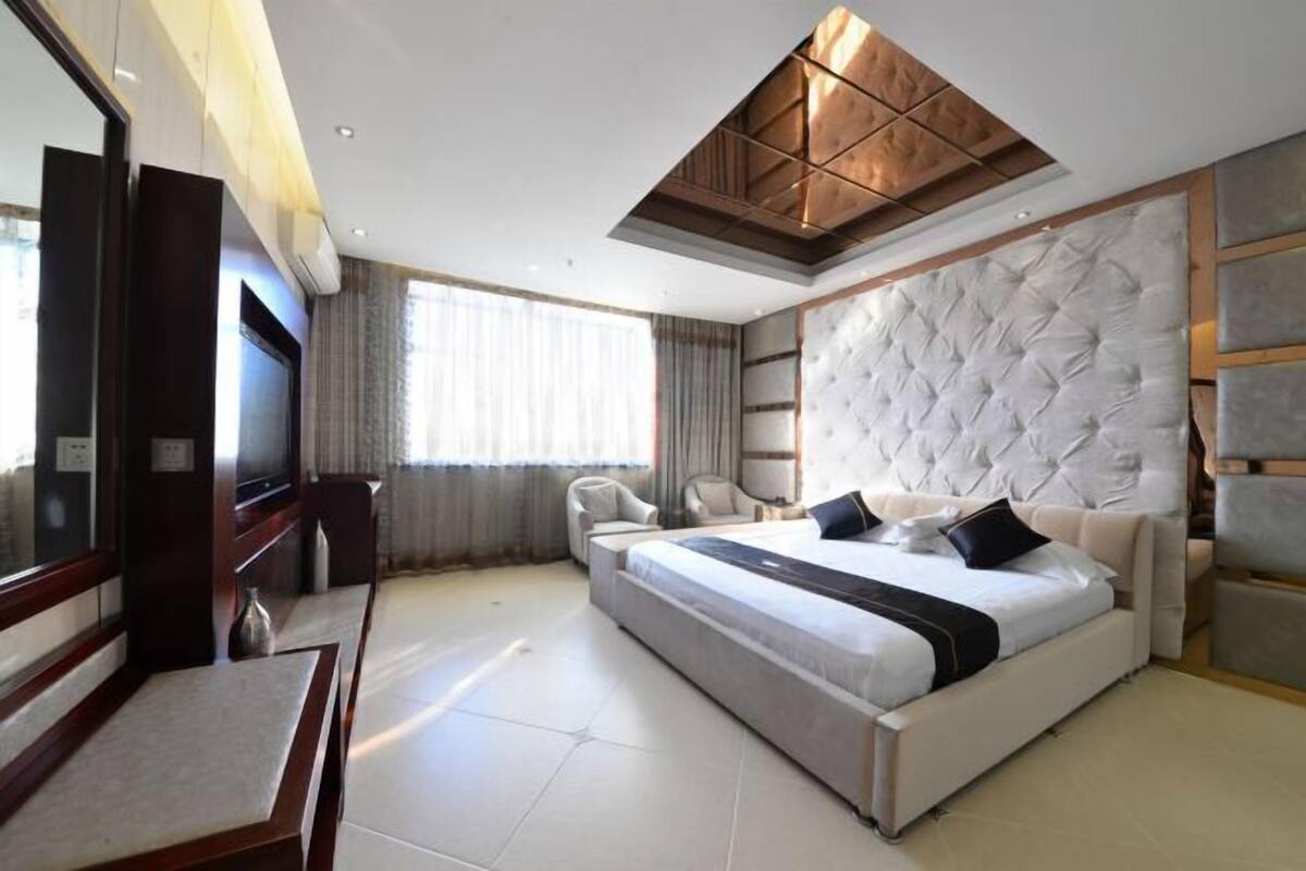 Una habitación de hotel moderna con una cama grande, un área de estar, un televisor y un techo de diseño único.