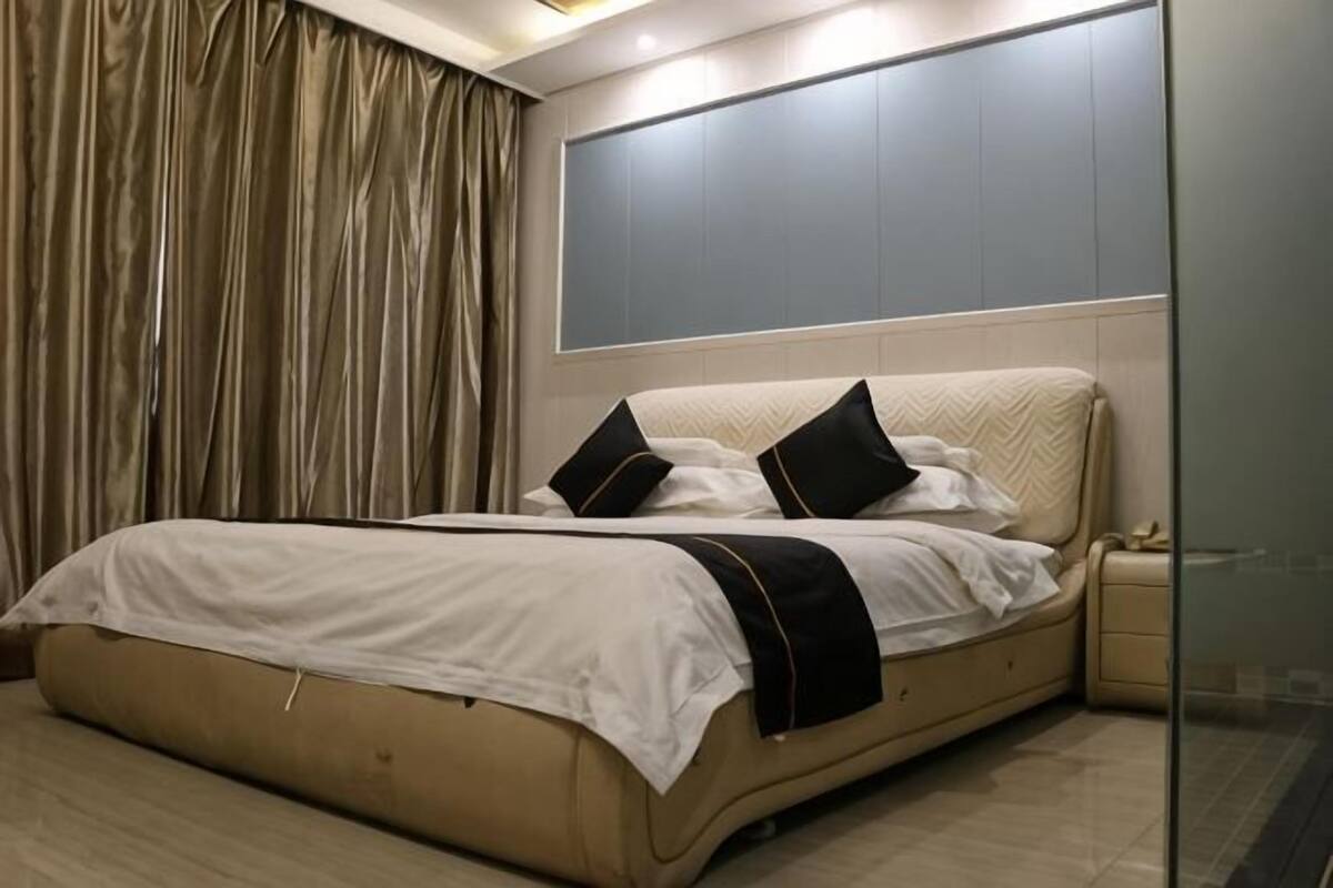 Un dormitorio con cama, cortinas, una mesita de noche y un panel en la pared.