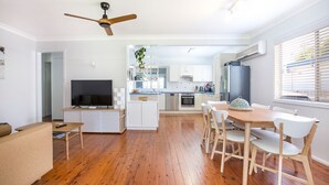 Une cuisine moderne avec des meubles blancs, une table à manger en bois et un ventilateur de plafond.
