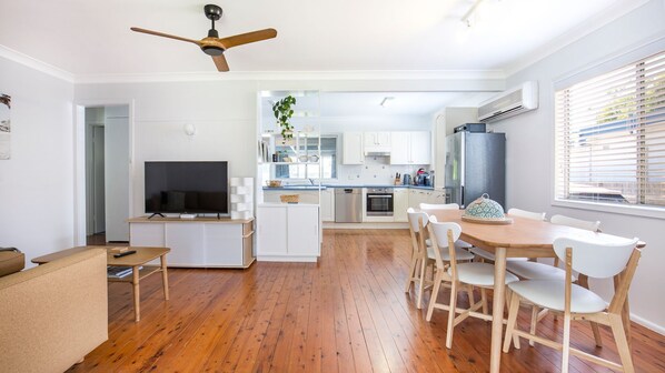 Une cuisine moderne avec des meubles blancs, une table à manger en bois et un ventilateur de plafond.