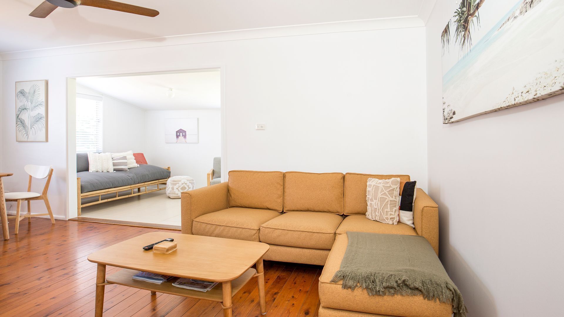A living room with a wooden floor, a beige sofa, a small wooden table, and a ceiling fan.