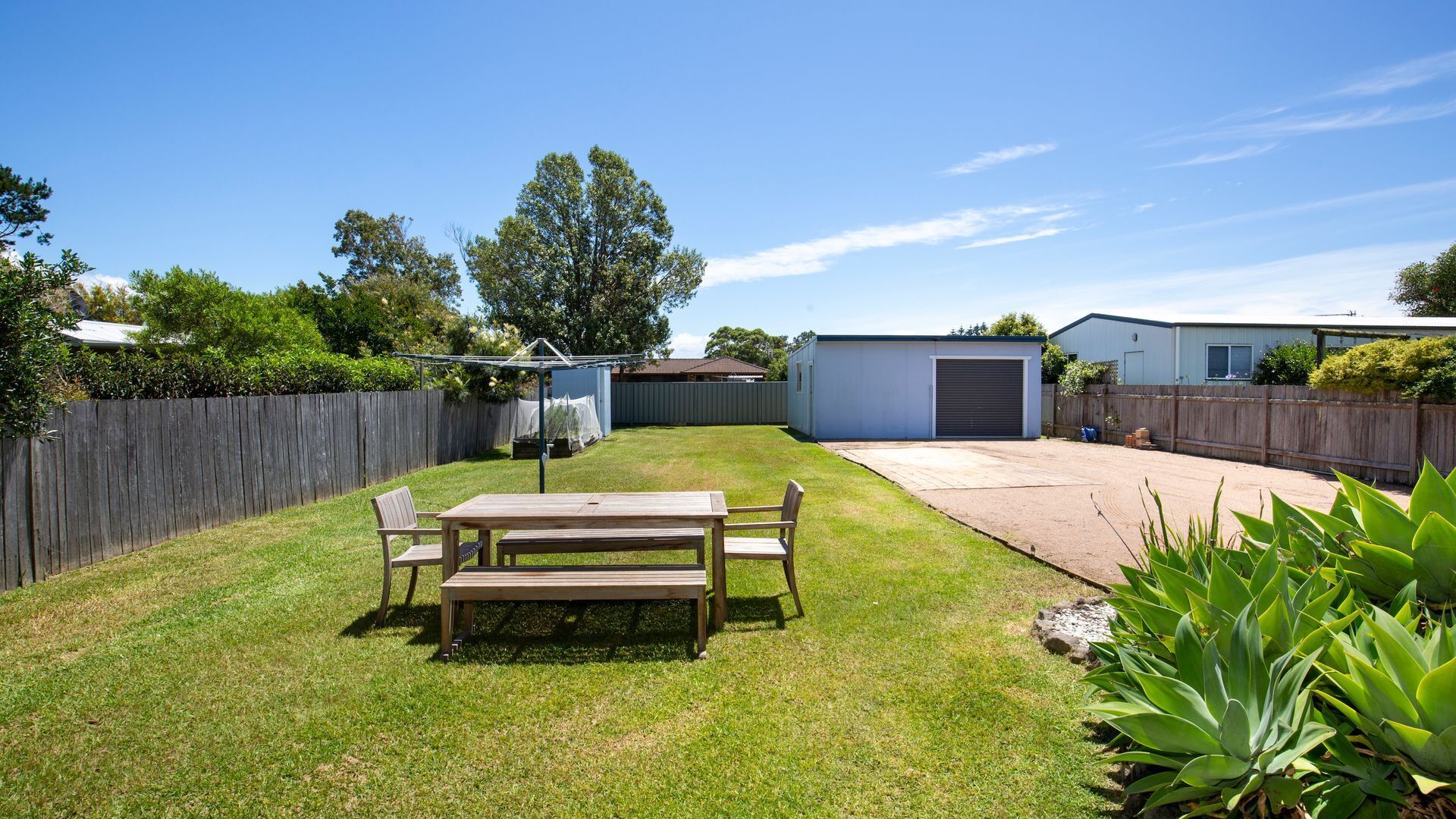 A backyard with a wooden table and chairs, a covered patio area, and a shed.