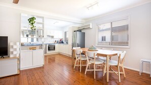 Une cuisine moderne avec des meubles blancs, un réfrigérateur en acier inoxydable et un coin repas comprenant une table en bois et des chaises blanches.