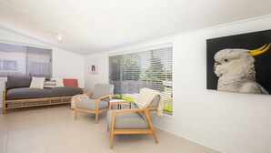 Un salon moderne avec un canapé, deux fauteuils et une grande fenêtre équipée de stores.