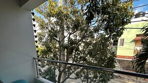 A balcony with green chairs, a railing, and a view of a tree and buildings. - New Two bedroom apartment, totally equipped with a large covered Patio (Santiago De Los Caballeros)