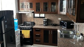 A kitchen with wooden cabinets, a stove, a sink, and a water dispenser. - New Two bedroom apartment, totally equipped with a large covered Patio (Santiago De Los Caballeros)