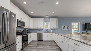 A modern kitchen with white cabinets, stainless steel appliances, a marble countertop, and a herringbone wood floor.