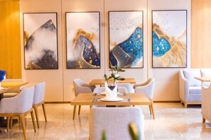 A hotel lobby with a dining area, four framed artworks on the wall, and a vase with a plant on the table. - Yuhe Hotel (Jiajiang)