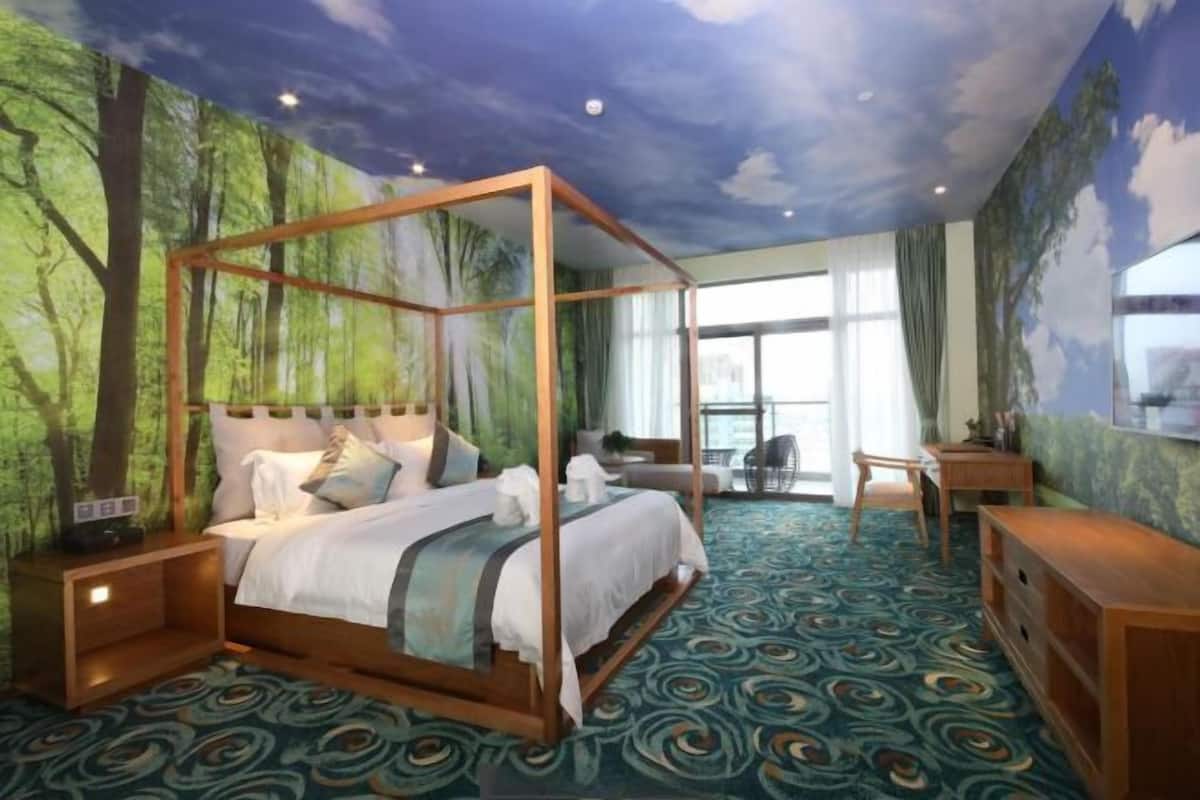 A four-poster bed with a canopy, a desk, and a chair in a room with a forest mural and patterned carpet.